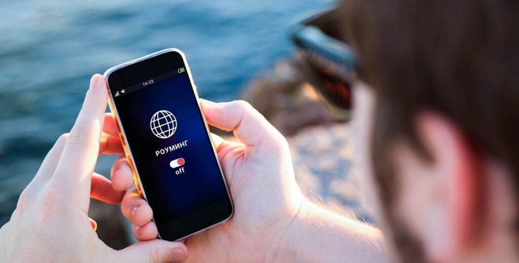 Россия блокирует белорусские SIM-карты — что происходит Человек держит смартфон с включённым экраном, на котором отображается надпись «Роуминг: off».