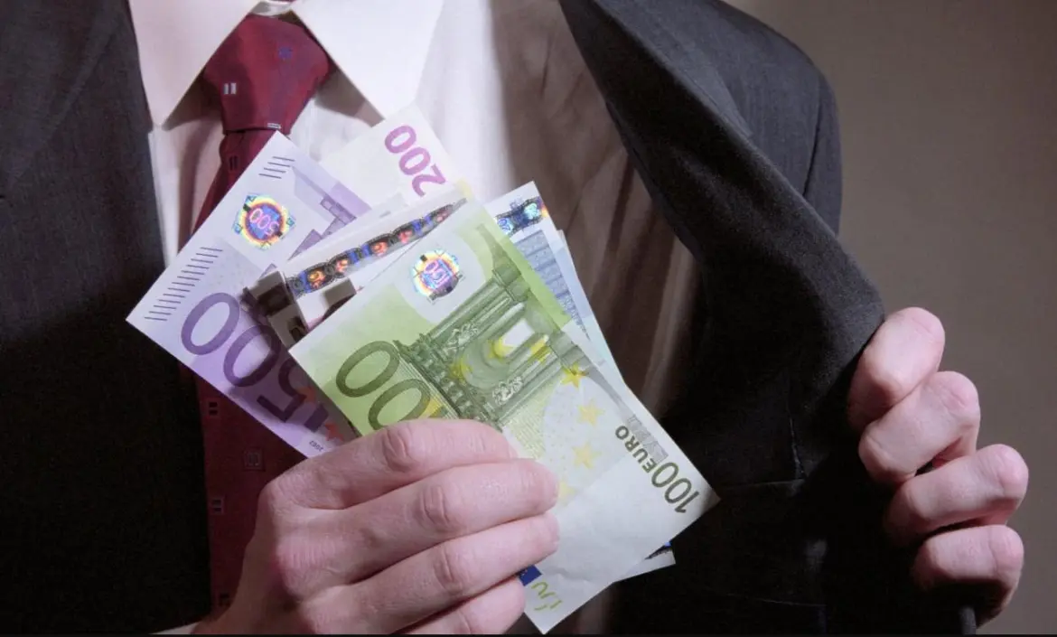 Три руководителя мясокомбината попались на взятках крупный план руки мужчины в деловом костюме, держащего банкноты евро и прячущего их во внутренний карман пиджака, банкрот